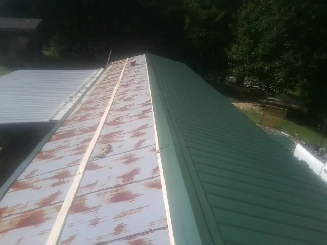Old rusted panels beside newly installed green metal roofing — Wind Damage Roof Repair by Roofing Brothers in Sharpsburg